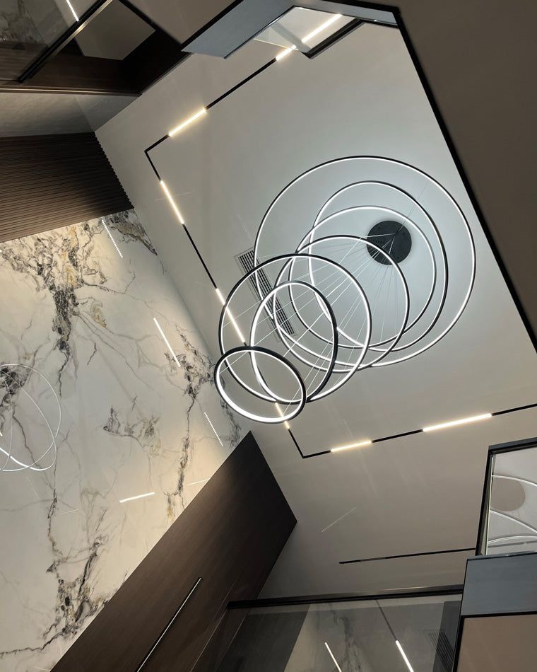 Shiny black ring chandelier viewed from below, creating crisp luminous circles and a striking monochrome look in a modern stairwell.