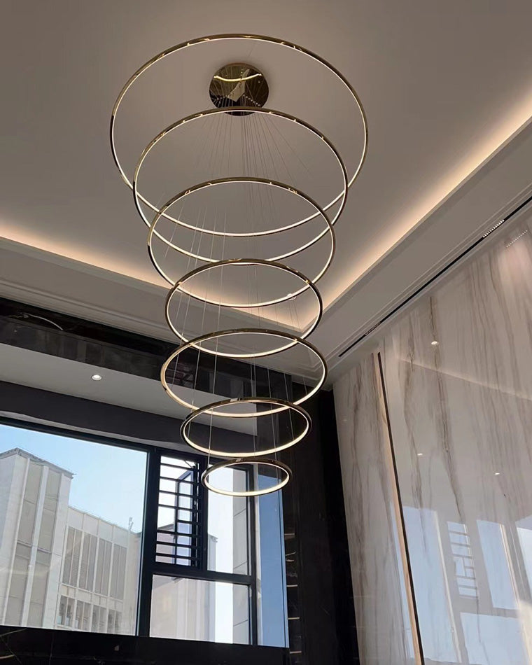 Unlit gold ring cascade beside tall windows, showing its elegant graduated silhouette and reflective finish in natural daylight.